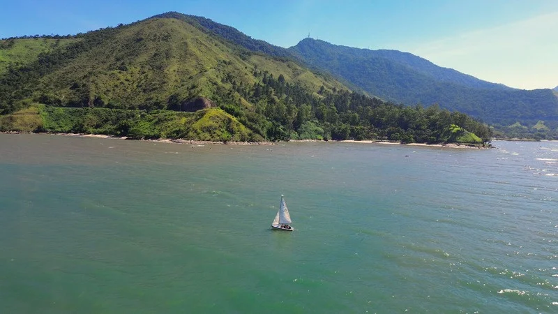 Um veleiro no mar diante das montanhas do Litoral Norte